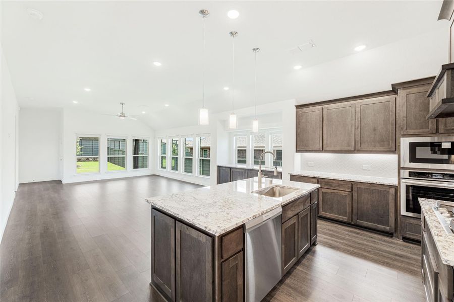 Open kitchen with dark wood cabinets, granite island, and stainless appliances opening to a bright living area with hardwood floors Open kitchen with dark wood cabinets, granite island, and stainless appliances opening to a bright living area with hardwood floors