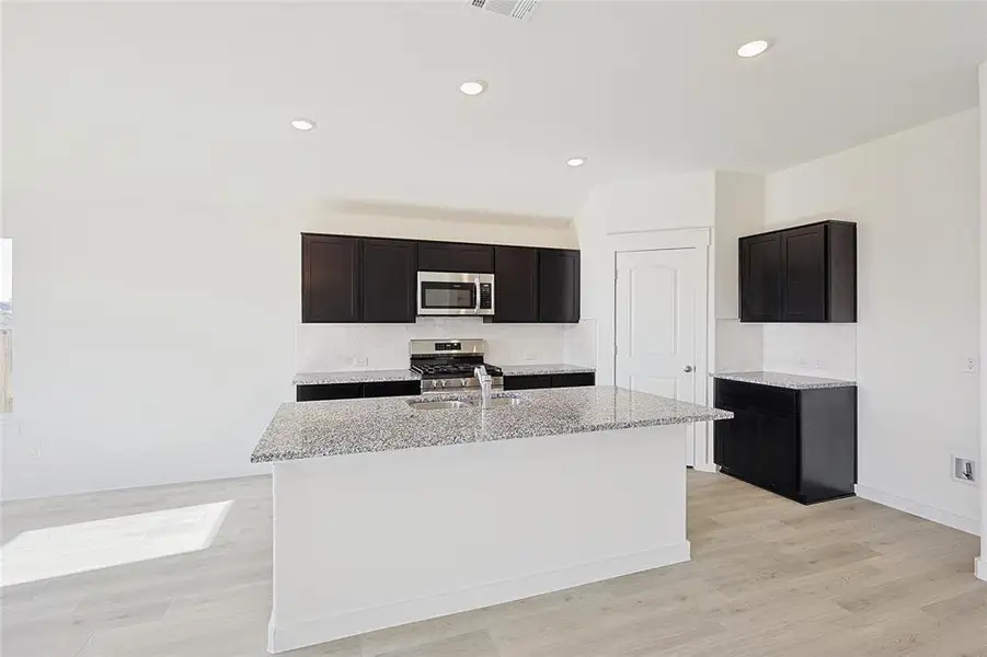 Kitchen featuring light stone counters, stainless steel appliances, sink, a center island with sink, and light hardwood / wood-style floors