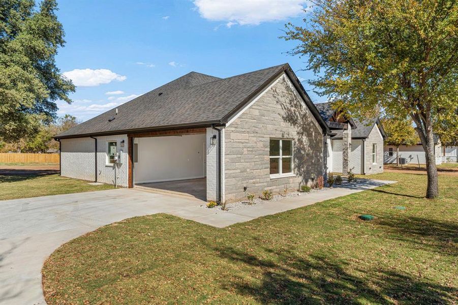 View of side of property featuring driveway, stone siding, a shingled roof, and a garage