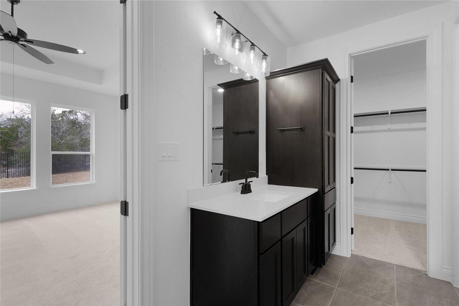 Bathroom with vanity, light colored carpet, a walk in closet, and ceiling fan