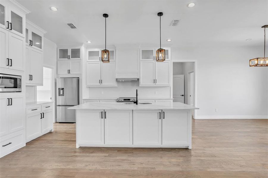 Kitchen with white cabinets, decorative light fixtures, light hardwood / wood-style flooring, and appliances with stainless steel finishes