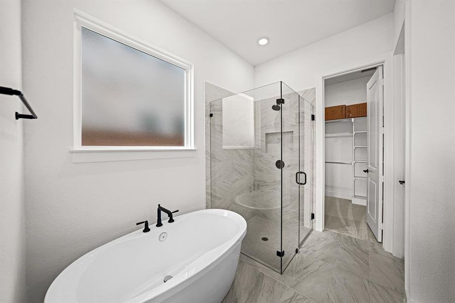 Full bathroom featuring a shower stall, a freestanding bath, light marble finish flooring, and a walk in closet