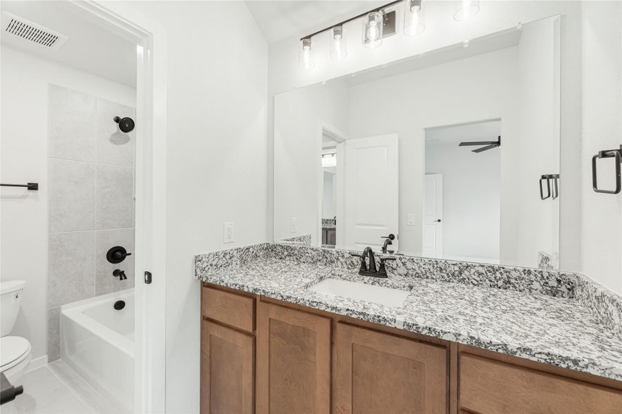 Bathroom with granite countertop vanity, wood cabinets, large mirror, and tiled tub-shower combo with black fixtures