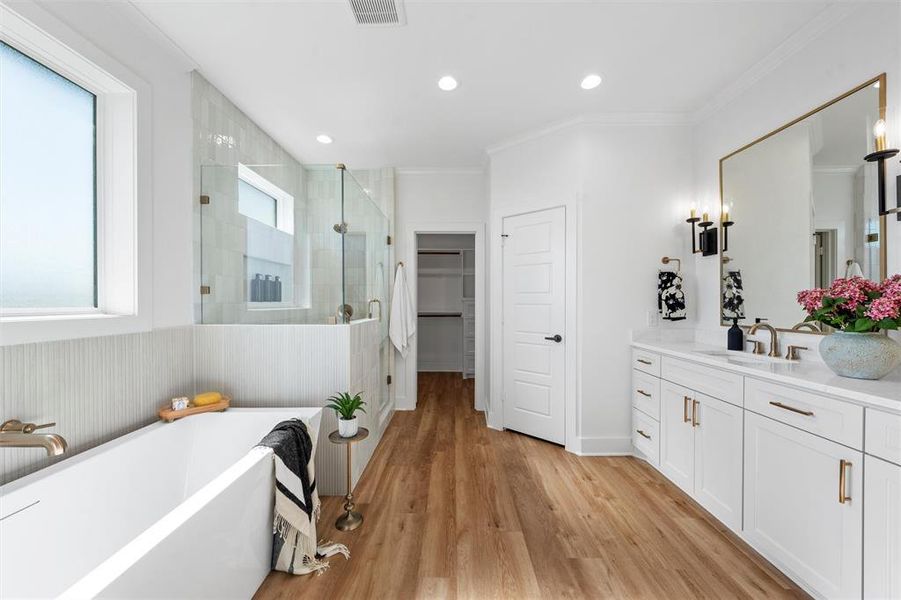 Full bath featuring a stall shower, vanity, a spacious closet, a soaking tub, and wood finished floors