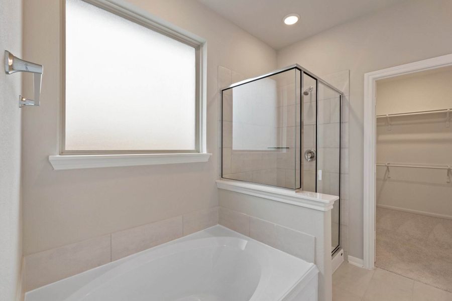 This additional view of your primary bathroom features tile flooring, fresh paint, walk-in shower, a separate garden tub, and a large walk-in closet.