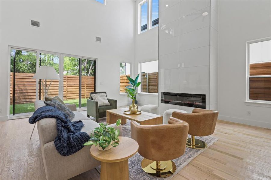 Living room featuring a tiled fireplace, a towering ceiling, and light wood-type flooring