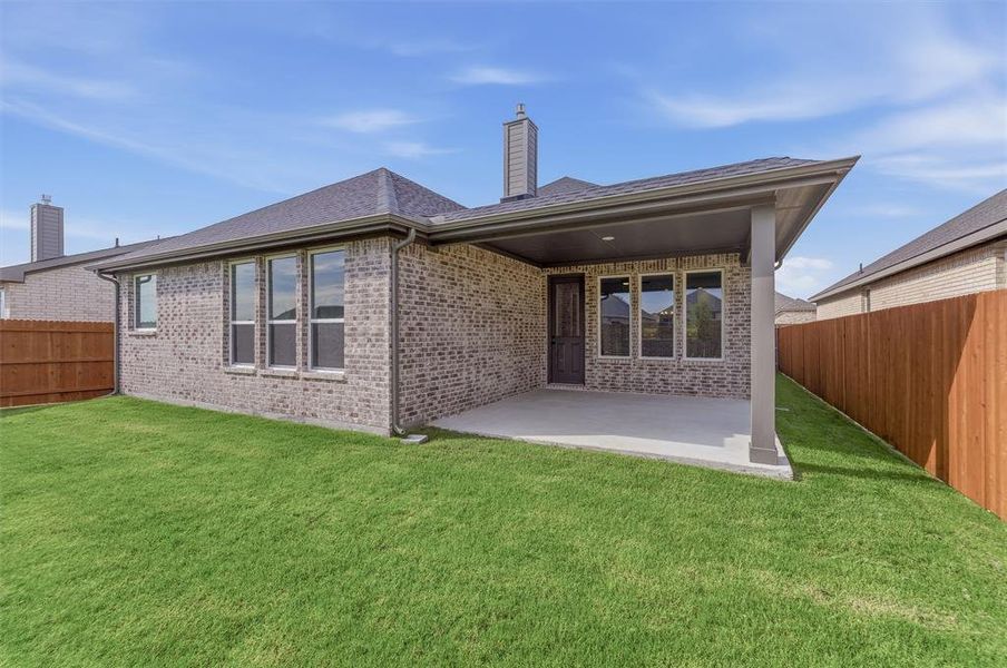 Expansive backyard featuring a manicured lawn, brick exterior, covered patio, and privacy fencing