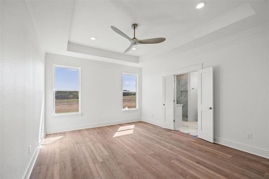 Spacious room featuring wood-finish flooring, a tray ceiling with recessed lighting and a ceiling fan, and two windows providing natural illumination