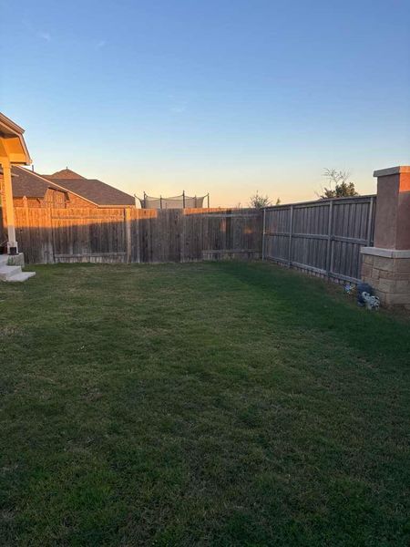 The property features a spacious lawn, enclosed by a wooden fence, with a stone column and partial stone wall visible on the right