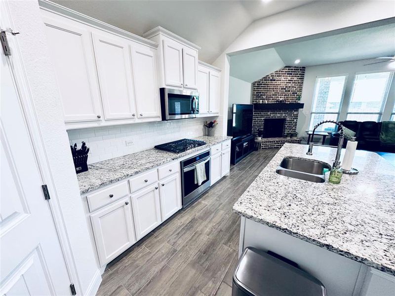 Kitchen featuring a fireplace, stainless steel appliances, decorative backsplash, hardwood / wood-style floors, and vaulted ceiling