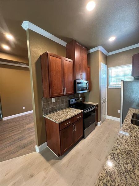 Kitchen with stove, light stone countertops, decorative backsplash, light hardwood / wood-style floors, and fridge