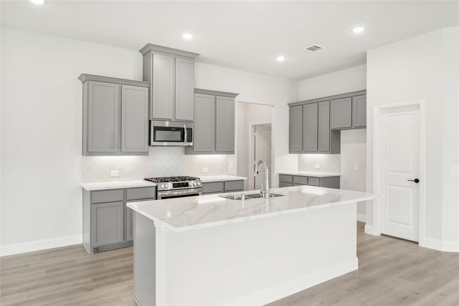 Kitchen with gray cabinets, large white quartz island with sink, and stainless steel appliances on light wood floors Kitchen with gray cabinets, large white quartz island with sink, and stainless steel appliances on light wood floors
