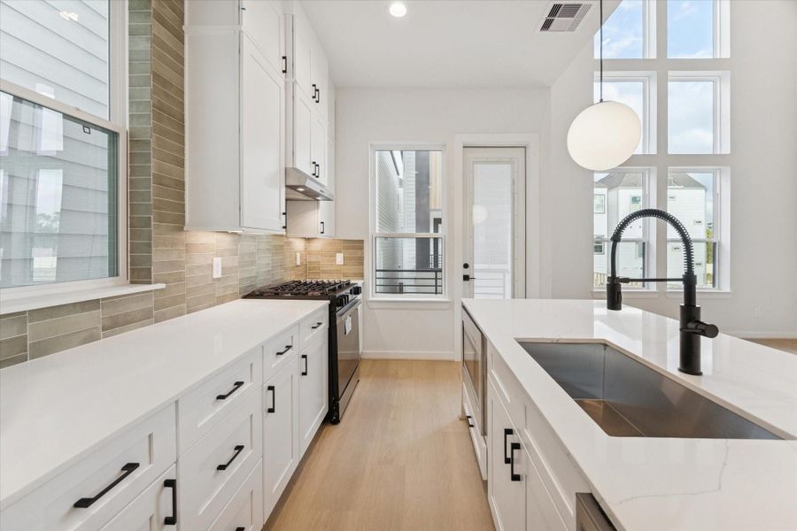 Another shot showcases the kitchen’s waterfall-edge island and sleek finishes, capturing how the space opens effortlessly to the living area and its impressive 20-ft ceilings, with the balcony door adding even more light and openness.
