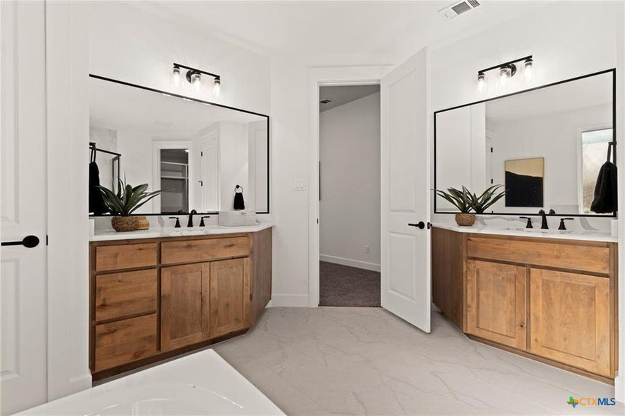 Full bathroom featuring two vanities, light marble finish flooring, and a tub