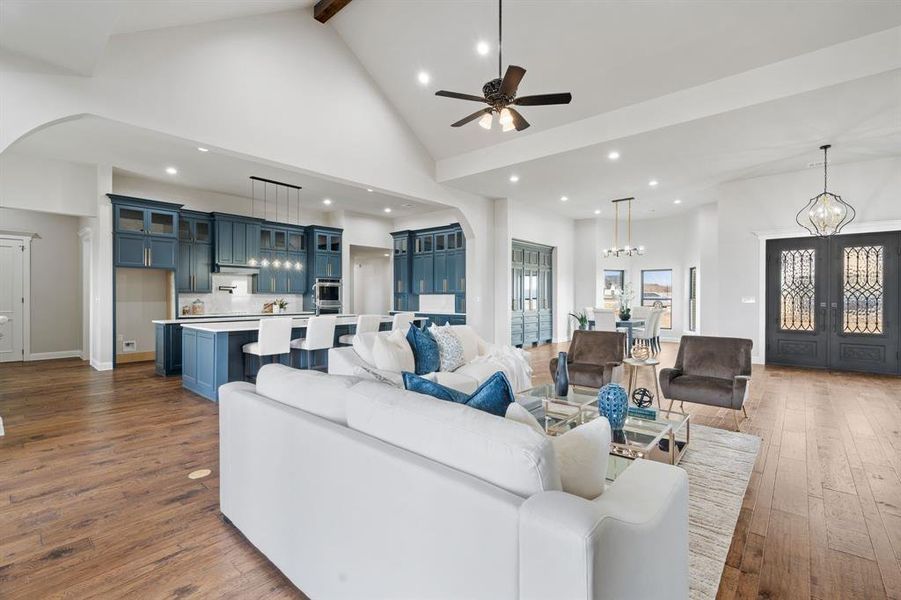 Living room with dark wood-type flooring, french doors, high vaulted ceiling, beam ceiling, and ceiling fan with notable chandelier