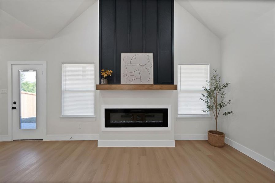 Unfurnished living room featuring a large fireplace, healthy amount of natural light, vaulted ceiling, and light wood finished floors Unfurnished living room featuring a large fireplace, healthy amount of natural light, vaulted ceiling, and light wood finished floors