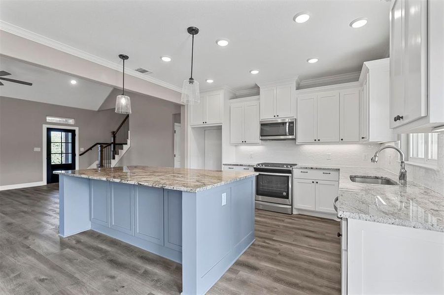 Kitchen with hanging light fixtures, sink, white cabinets, a kitchen island, and stainless steel appliances