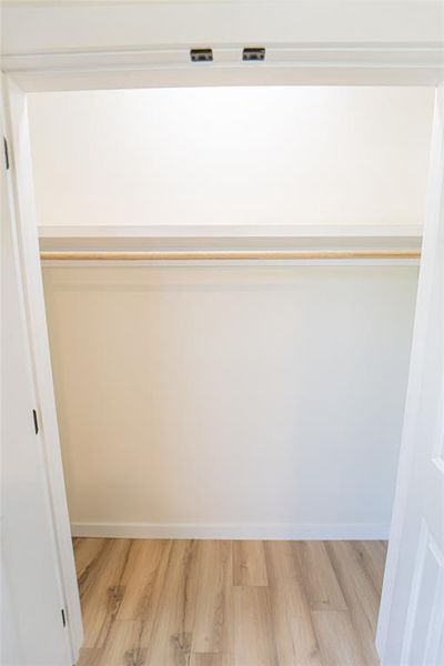 Closet space featuring wood-finish flooring, a single hanging rod, and an upper shelf, framed by white paneled doors