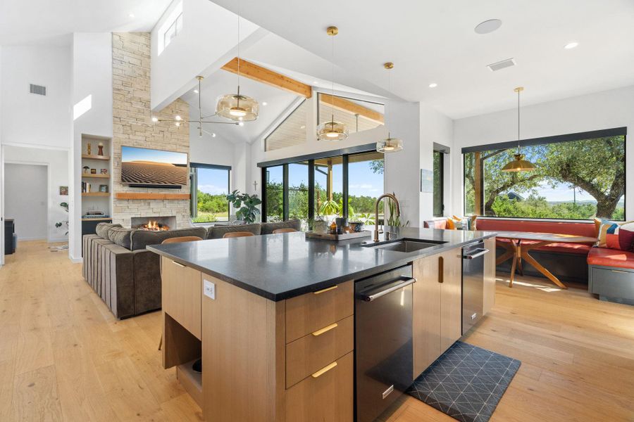 Spacious open-concept living area featuring a kitchen island with sink and integrated appliances, a stone-clad fireplace, and high vaulted ceilings with exposed beams