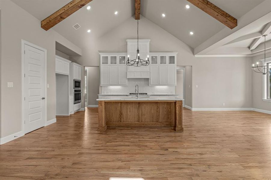 Kitchen featuring a large island, white cabinets, tasteful backsplash, and a chandelier