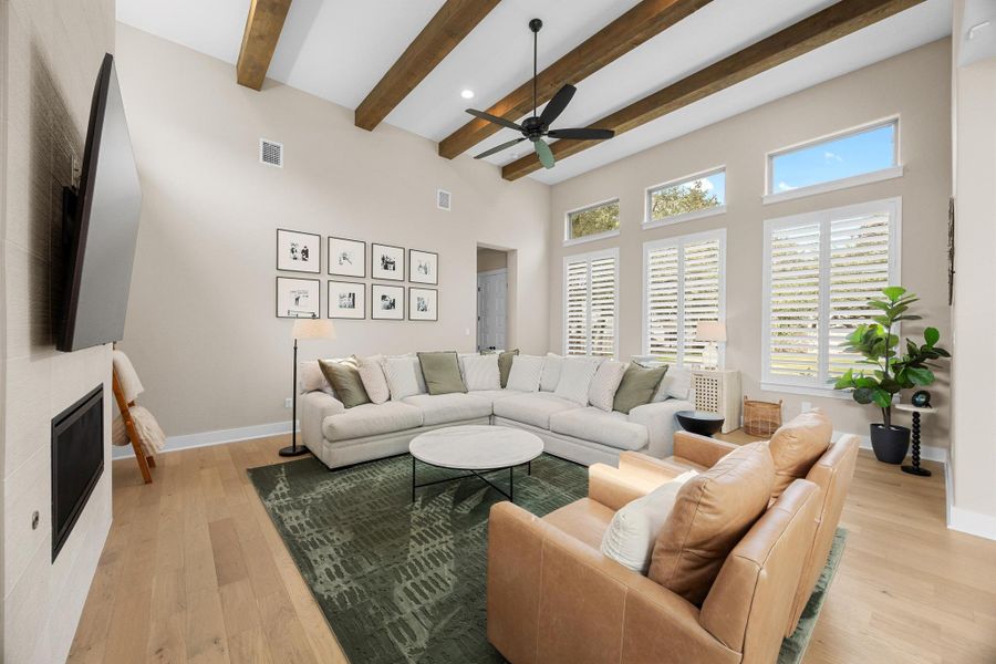 Living room featuring a glass covered fireplace, beam ceiling, light wood-style floors, a ceiling fan, and recessed lighting
