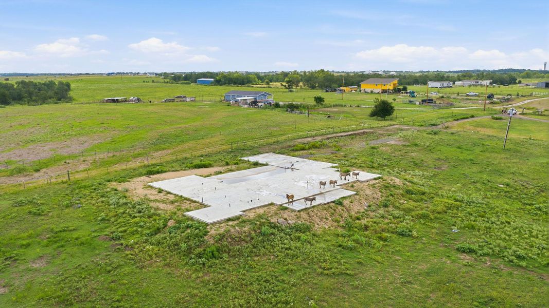 A rural setting with a new foundation awaiting construction, surrounded by open pastures.