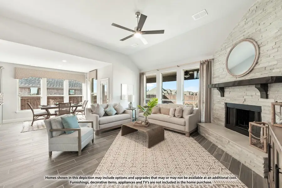 Living room with vaulted ceiling, stone fireplace, ceiling fan, and open view to dining area with large windows. Living room with vaulted ceiling, stone fireplace, ceiling fan, and open view to dining area with large windows.