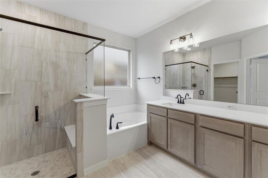Bathroom featuring a spacious walk-in shower with a built-in bench, a separate soaking tub, and a dual vanity with a quartz countertop