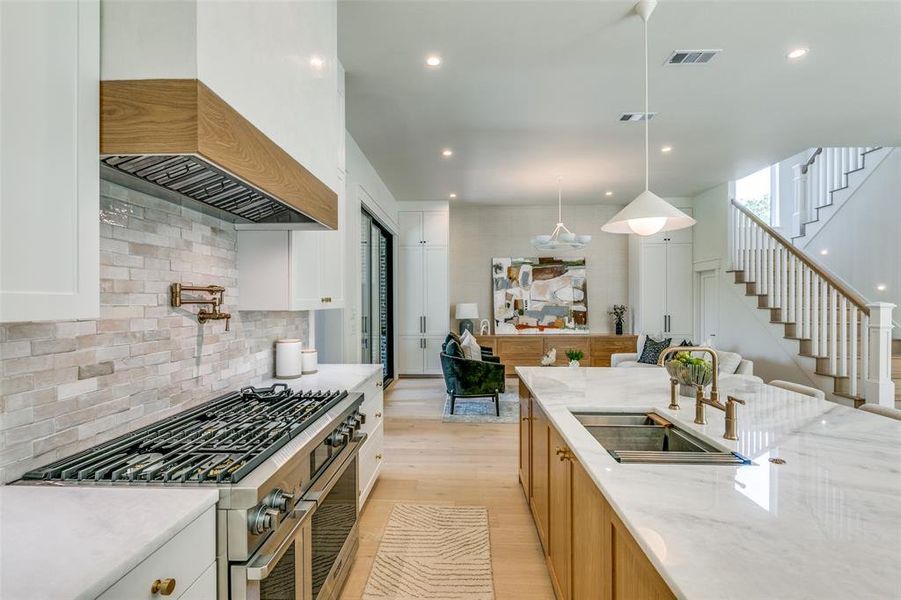 Kitchen with range with two ovens, light hardwood / wood-style flooring, light stone counters, premium range hood, and backsplash