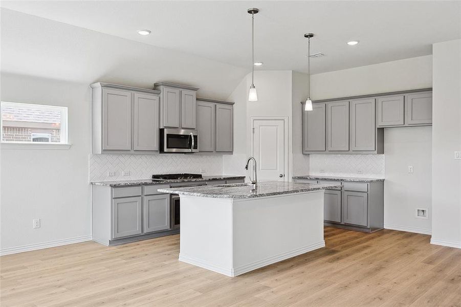 Kitchen featuring backsplash, light stone countertops, appliances with stainless steel finishes, and light hardwood / wood-style floors