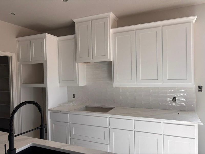 Kitchen with white cabinetry, light stone counters, and tasteful backsplash Kitchen with white cabinetry, light stone counters, and tasteful backsplash