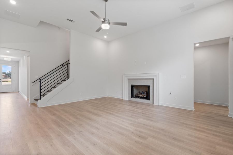 Wood-finish flooring throughout, featuring a fireplace with a white mantel, a modern ceiling fan, and recessed lighting Wood-finish flooring throughout, featuring a fireplace with a white mantel, a modern ceiling fan, and recessed lighting