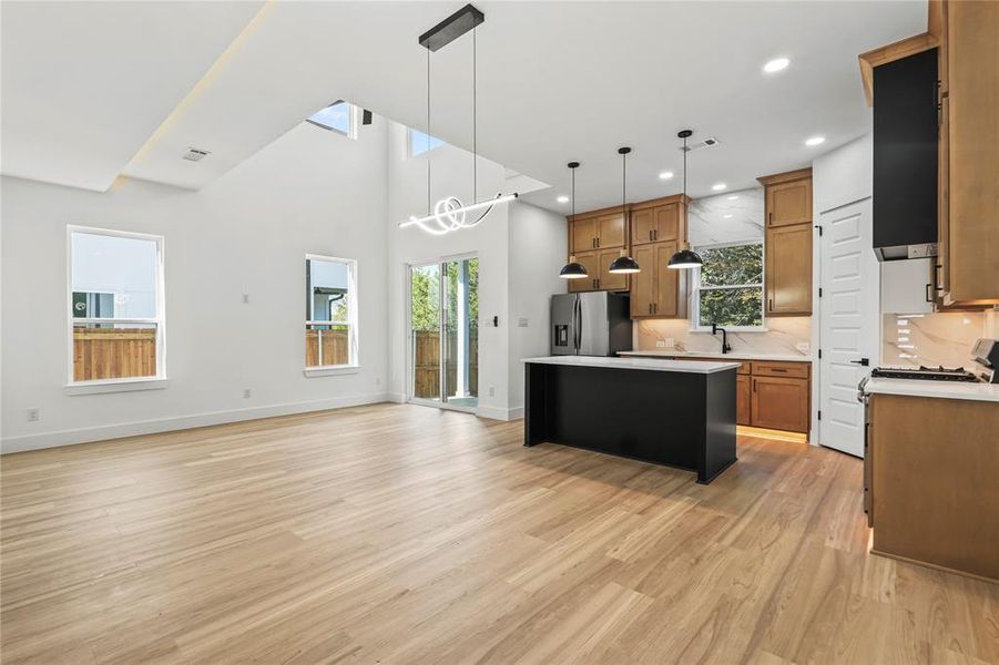 Kitchen featuring open floor plan, pendant lighting, a center island, brown cabinets, and a high ceiling