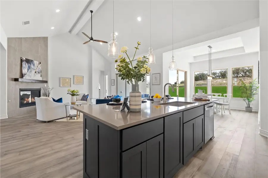 Kitchen featuring beam ceiling, open floor plan, light wood-style flooring, a tiled fireplace, and a center island with sink