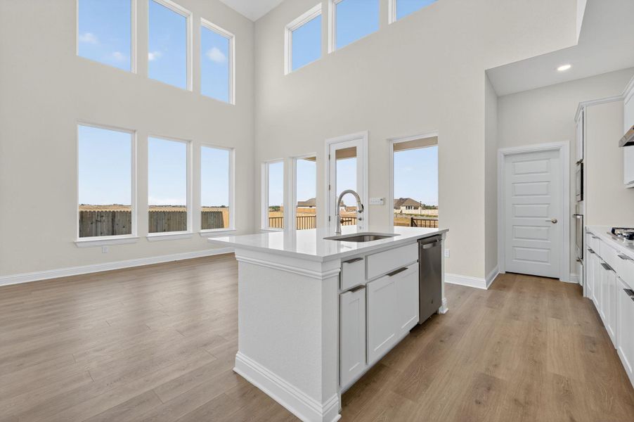 Kitchen with white cabinetry, a center island with sink, light stone countertops, light wood finished floors, and a high ceiling