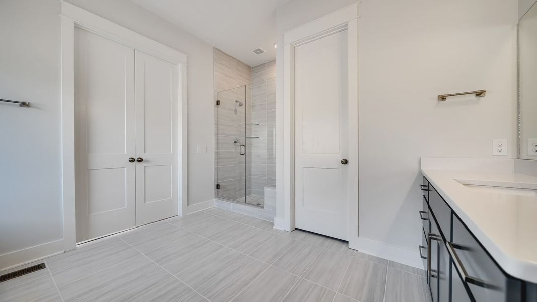Large tiled bathroom with multiple vanities, glass shower enclosure, and freestanding tub