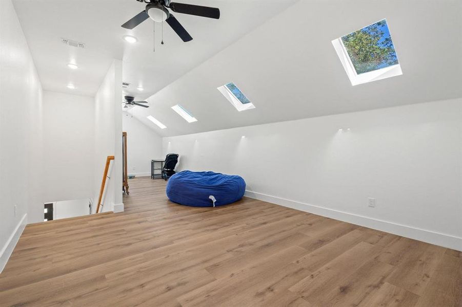 Additional living space featuring vaulted ceiling, a skylight, light wood-style floors, and ceiling fan