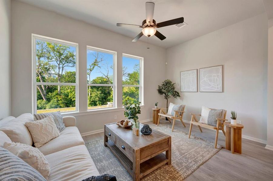 Bright living area featuring a trio of large windows, wood-finish flooring, a contemporary ceiling fan, and light neutral wall tones