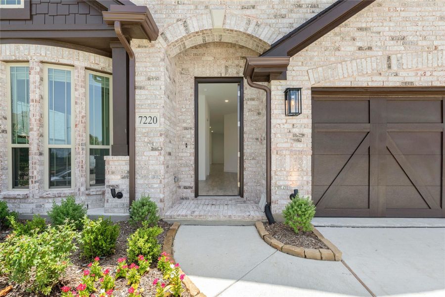 Front entry of brick home with arched doorway, glass door, wall sconce, and attached garage Front entry of brick home with arched doorway, glass door, wall sconce, and attached garage