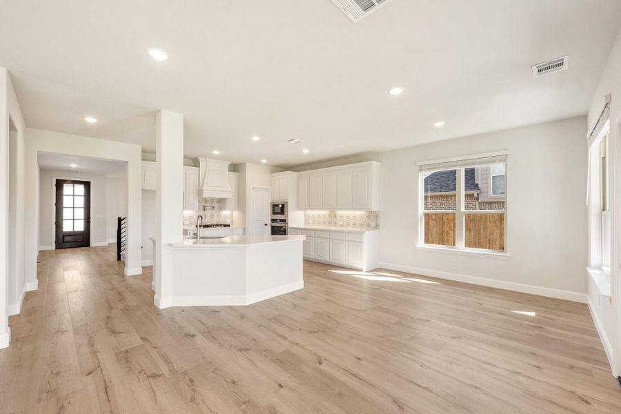 Open-concept living area and kitchen with white cabinets, curved island, and light hardwood floors