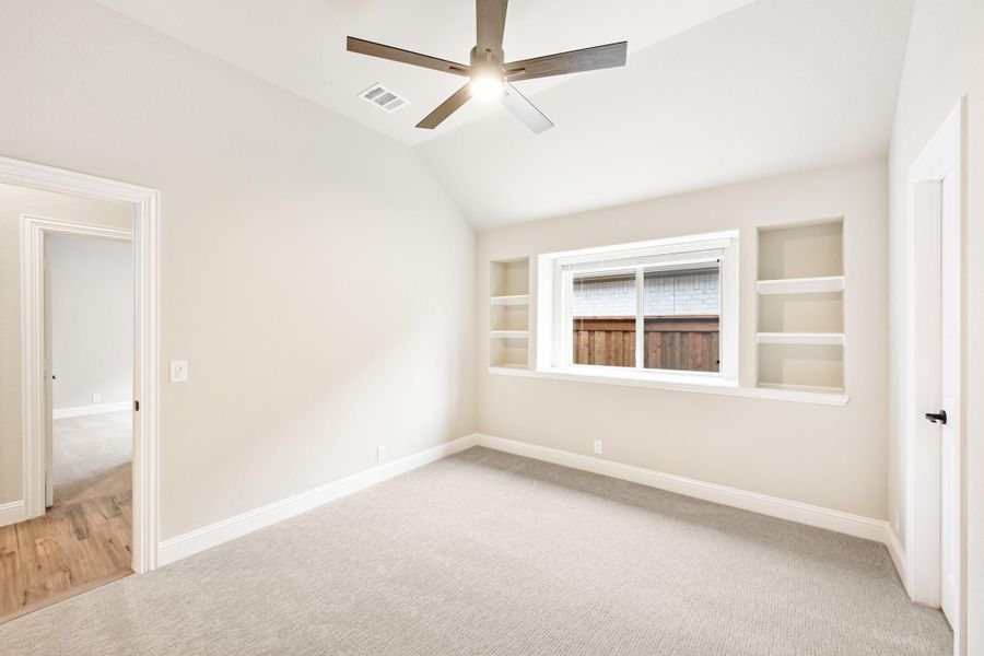 Empty bedroom with carpet, vaulted ceiling, ceiling fan, and built-in shelves flanking a window Empty bedroom with carpet, vaulted ceiling, ceiling fan, and built-in shelves flanking a window