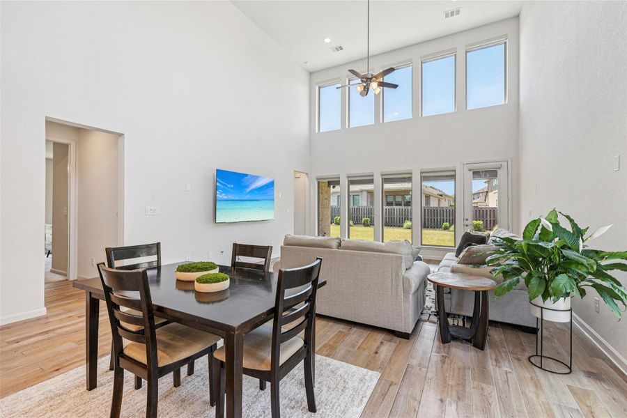 This inviting living space features high ceilings, light wood-style flooring, and large windows providing ample natural light and views of the backyard