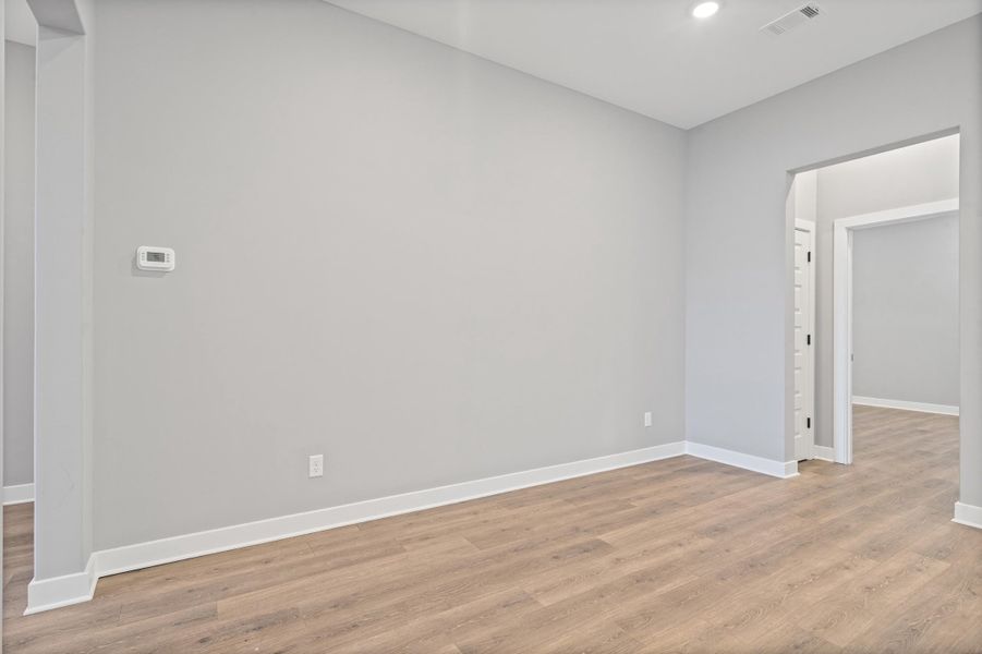 Interior room featuring light gray walls, wood-finish flooring, white baseboards, a recessed ceiling light, and a digital thermostat Interior room featuring light gray walls, wood-finish flooring, white baseboards, a recessed ceiling light, and a digital thermostat