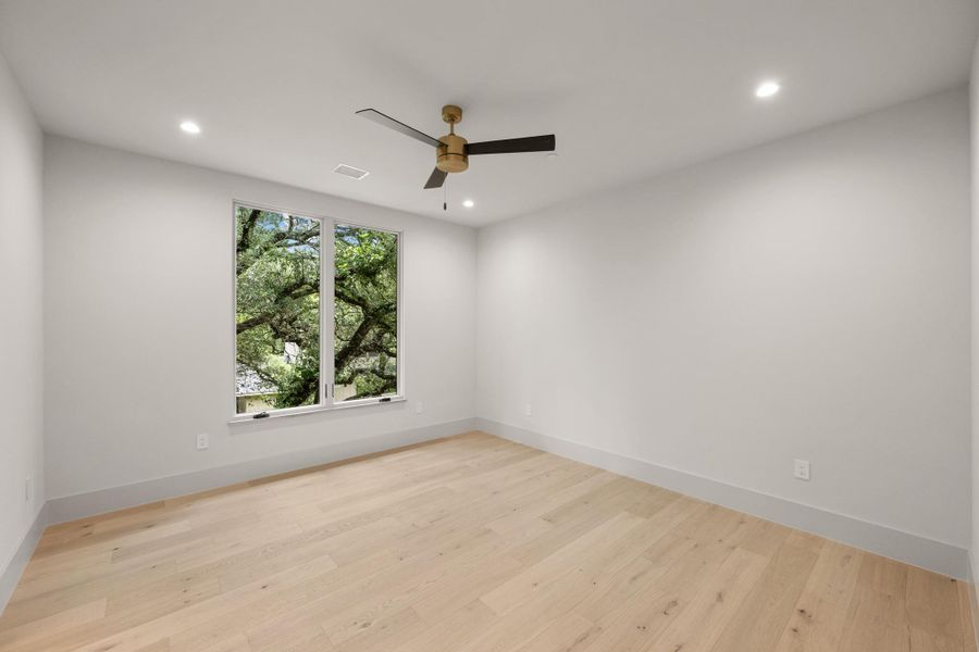 A quiet bedroom showcases light wood flooring and a refreshing view of mature trees. A quiet bedroom showcases light wood flooring and a refreshing view of mature trees.