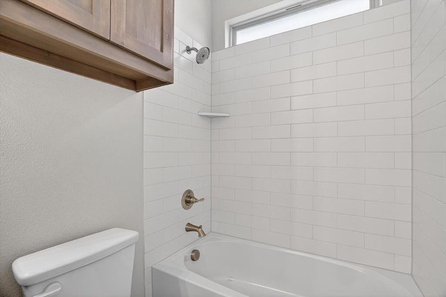 Bathtub and shower combination featuring subway tile surround, brushed nickel fixtures, a built-in shelf, and an upper transom window