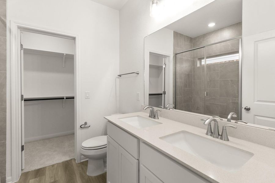 The bathroom features a double vanity with stone countertops, a large mirror, and a shower with a glass enclosure and tiled walls