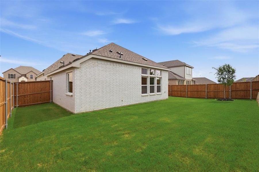 Expansive backyard featuring a lush lawn, privacy fencing, and a mature tree