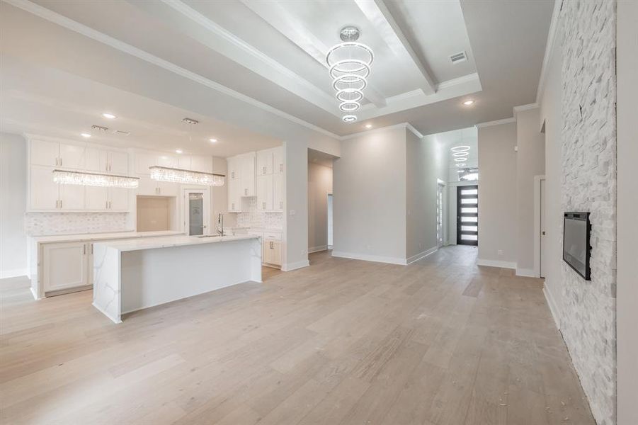 Unfurnished living room featuring light wood finished floors, a chandelier, crown molding, recessed lighting, and a fireplace