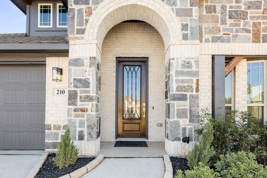 Front entry with stone arch, wood and iron door, brick exterior, and landscaped walkway Front entry with stone arch, wood and iron door, brick exterior, and landscaped walkway