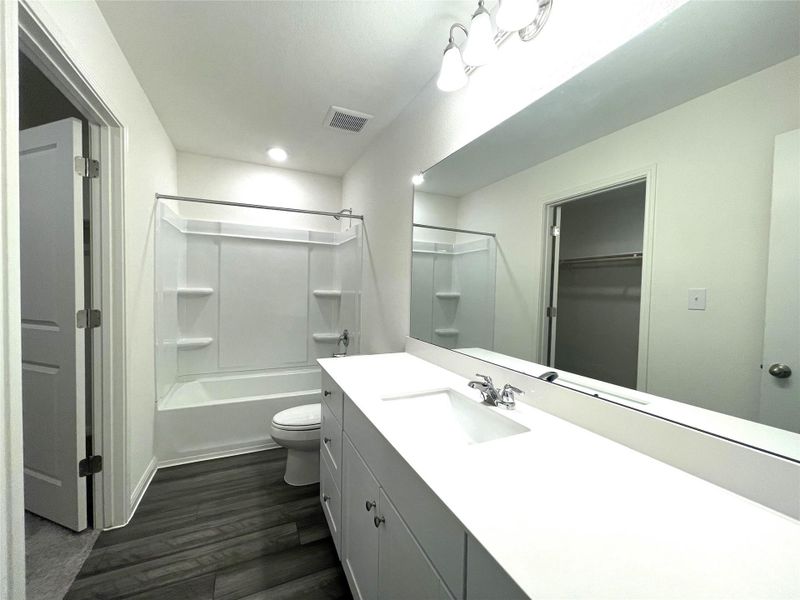 Bathroom featuring vanity, washtub / shower combination, wood finished floors, visible vents, and toilet